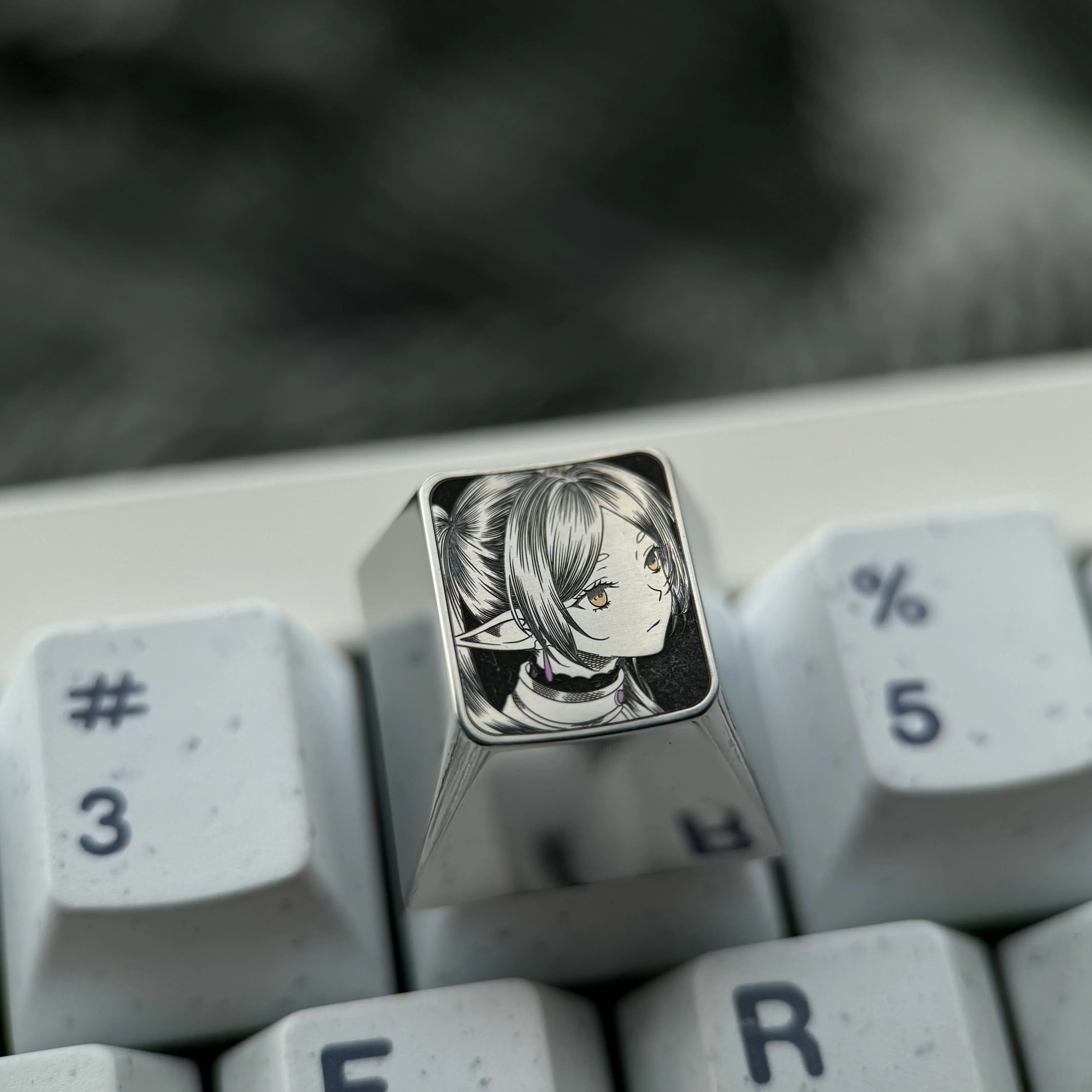 Gallery of the hand-sculpted titanium Frieren keycap, showcasing the precision-carved anime portrait and intricate stippling from various angles.