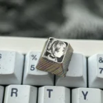 Multiple views of the hand-sculpted titanium Frieren keycap, revealing the precision-carved anime portrait and mirror-finish with intricate stippling.