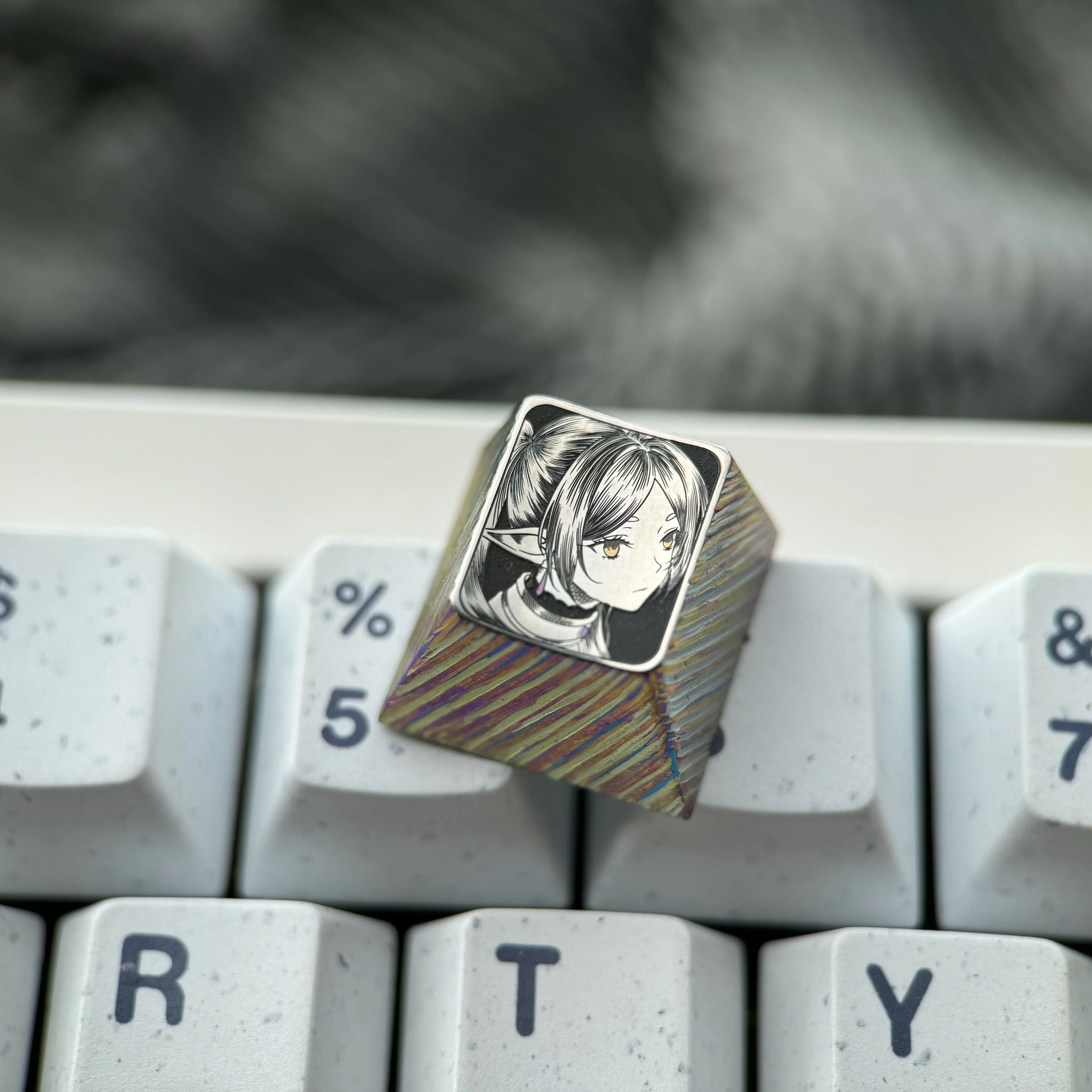 Multiple views of the hand-sculpted titanium Frieren keycap, revealing the precision-carved anime portrait and mirror-finish with intricate stippling.