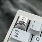 Precision-engraved 2B Titanium Keycap for mechanical keyboards, showcasing iconic Nier Automata character art and artisan metallic finish.