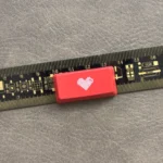 A premium Double-Shot ABS Backlit Heart Keycap, viewed from a slight angle, showcasing its glowing red translucent heart on a sleek red design.