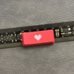 Premium double-shot ABS backlit heart keycap from various angles. Reveals its sleek black/red finish, translucent glowing heart icon.