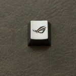 Close-up views of the ROG Logo Alloy Keycaps, showcasing its aggressive angular design in a premium metallic finish from various angles.