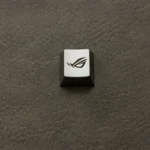 A single, exclusive silver ROG Logo Alloy Keycaps, meticulously crafted with an aggressive, angular design for magnetic switches, embodying powerful stye.