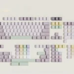 A collection of Taro Pistachio PBT keycaps set showcasing their sweet pastel purple, green, and cream dessert-inspired design from various angles.