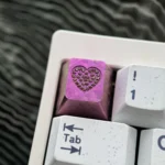 Close-up of a handcrafted RGB titanium keycap, showcasing its sparkling gemstone heart inlay and intricate custom engraving.