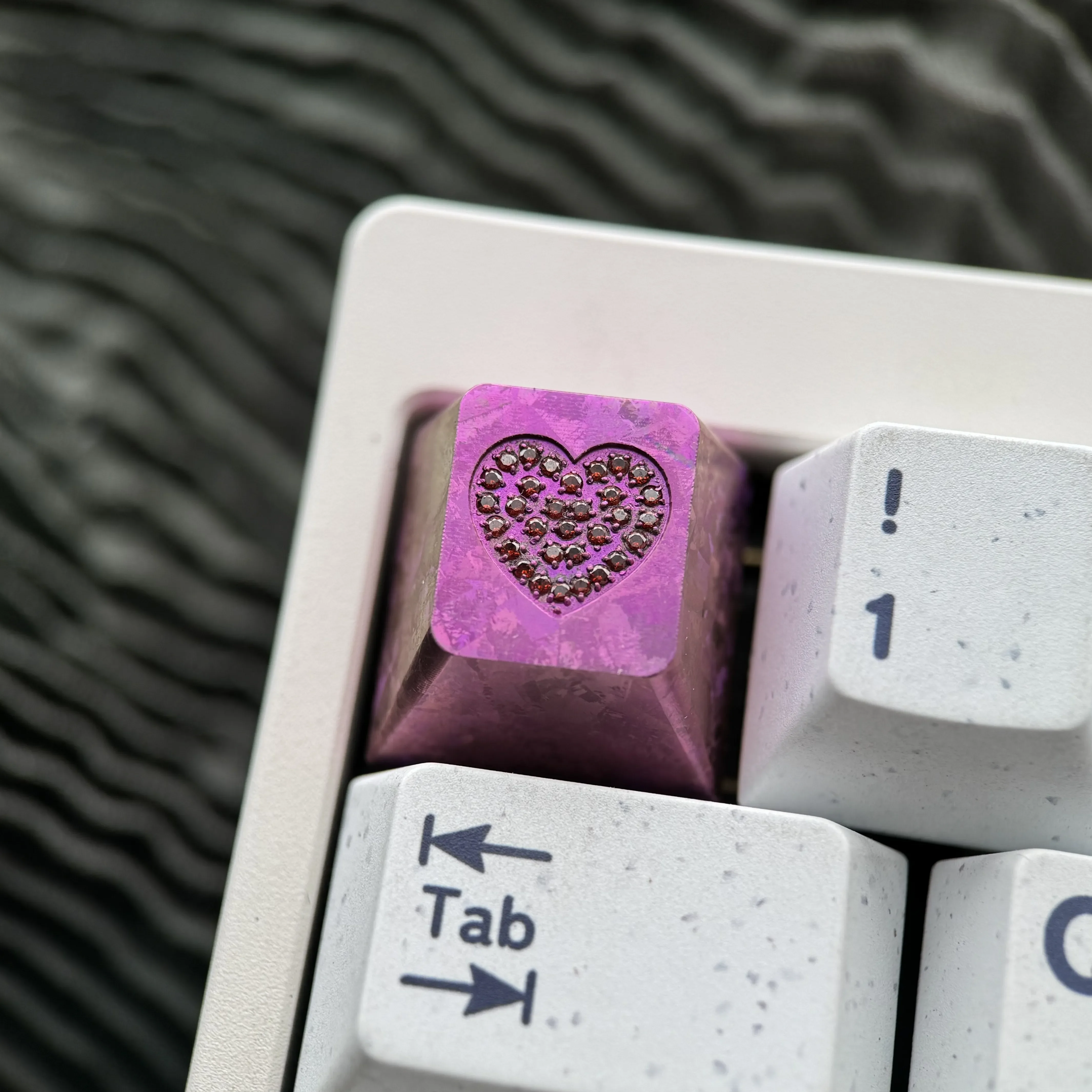 Close-up of a handcrafted RGB titanium keycap, showcasing its sparkling gemstone heart inlay and intricate custom engraving.