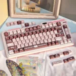 Elegant Coffee Whisper PBT Keycap Set, showcasing durable dye-sub PBT keycaps with smooth textures in a warm coffee and rose palette.