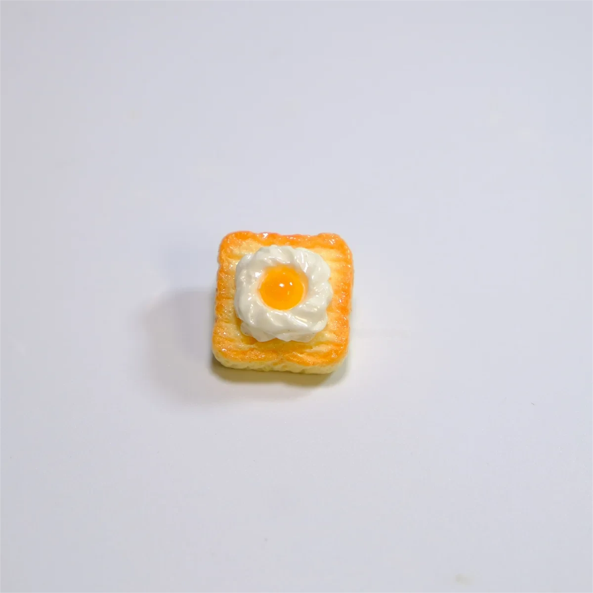 Close-up of a whimsical handcrafted 3D fried egg toast artisan keycap, showing its vibrant yellow yolk and white toast details from multiple angles.
