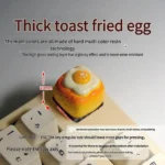 Close-up views of the whimsical handcrafted 3D fried egg toast artisan keycap, showcasing its vibrant yellow and white details from multiple angles.