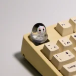 A cute handmade artisan glowing No-Face keycap, featuring its whimsical translucent 3D design and ethereal glow from different angles on a mechanical keyboard.