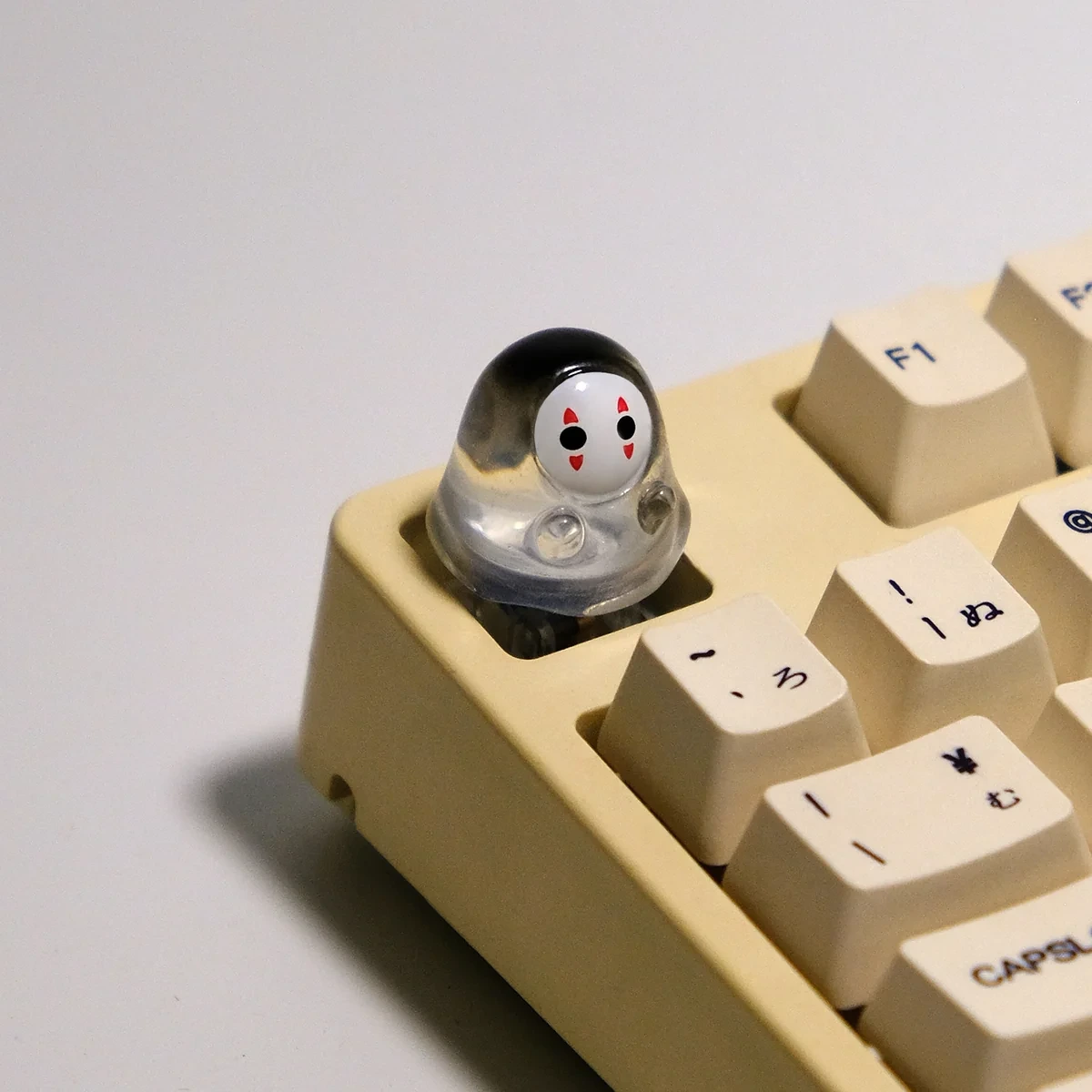 A cute handmade artisan glowing No-Face keycap, featuring its whimsical translucent 3D design and ethereal glow from different angles on a mechanical keyboard.