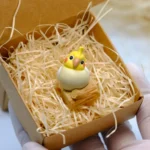 Whimsical handcrafted 3D cockatiel artisan keycap. It's vibrant, on a wooden stump with green grass and pink peonies.