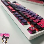 Mischievous Kuromi RGB Pudding Keycaps Set, showcasing iconic designs in vibrant purple/pink. Dazzling RGB glow from a distinct angle.