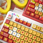 A playful set of McDonald's MOA PBT keycaps set displayed from various angles, showcasing vibrant red, yellow, and white colors with iconic fast-food design.