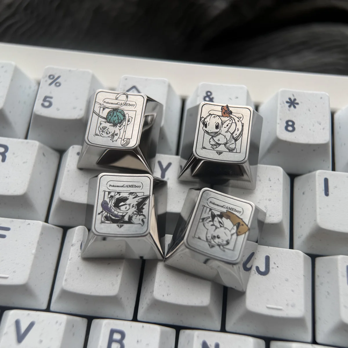 Close-up views of the premium Characters Titanium Pokemon Artisan Keycap, showcasing its lustrous iridescent and sleek polished titanium finishes from various angles.