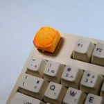 Close-up gallery views of a playful, handcrafted orange artisan keycap for mechanical keyboards, sculpted like a miniature whimsical orange fruit.