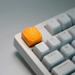 Close-up of a handcrafted, whimsical orange artisan keycap for keyboards, showcasing its vibrant miniature fruit design from multiple angles.