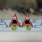 Whimsical handmade Patrick Star keycap crafted from pink resin, shown from various playful angles, highlighting its detailed artisan design.