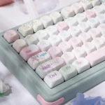 The Wind Chime Dream PBT Keycap Set from an artistic angle, showcasing durable PBT and ethereal blue-pink gradient with whimsical wind chime and cloud art.