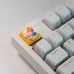 Close-up of a handmade, hyper-realistic Strawberry Mille-Feuille Artisan Keycap from various angles, showcasing its vibrant pink and cream layers.