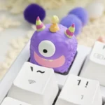 A playful handcrafted artisan resin keycap featuring a whimsical monster, viewed from a side angle to highlight its intricate translucent layers.
