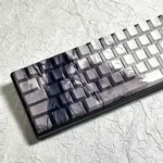 Angled view: Artistic Bamboo Rain PBT Keycaps Set. Unique side-lit design with serene bamboo forest, falling rain, and original character subtly glowiing.