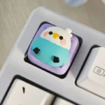 Multiple playful views of a vibrant, whimsical handcrafted parakeet resin keycap, showcasing its intricately layered design as a unique keyboard accent.