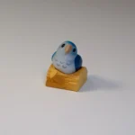 Hand-sculpted Monk Parrot artisan keycap, vibrant and whimsical, from an alternate view, highlighting intricate 3D details. Charming handcrafted keyboard.