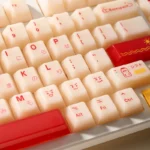 Playful Yakult keycap set gallery: unique artisan desk art shown from various angles. Whimsical bottle design in warm red and beige, evoking nostalgic charm.