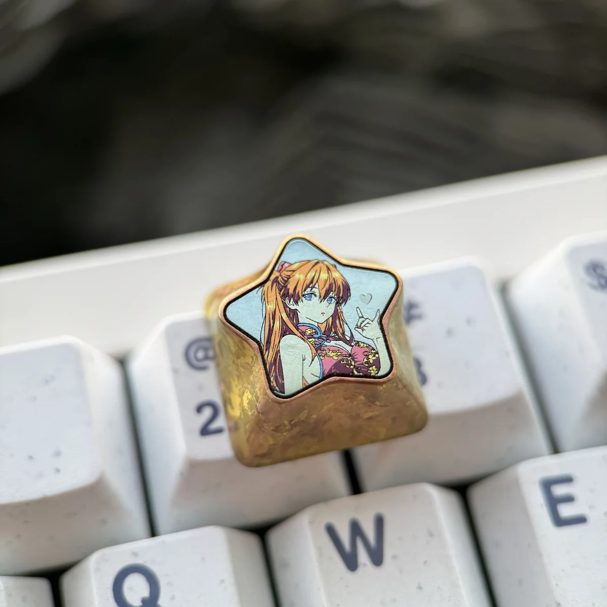 A premium titanium Asuka Langley Soryu keycap, featuring its iconic fiery design with a striking star pentagon and polished finish, displayed from multiple angles.