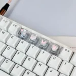 An angled view of high-transparency 3D pink butterfly artisan keycaps, showcasing delicate butterflies and hearts for a dreamy, whimsical WASD keyboard.