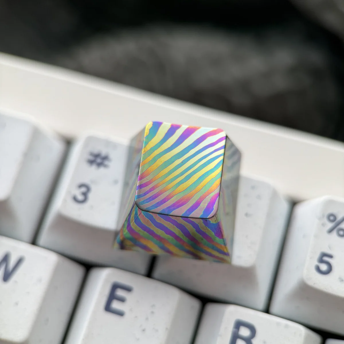 Unique handcrafted Damascus titanium ESC keycap shown from various angles, highlighting its intricate patterns and iridescent hues.