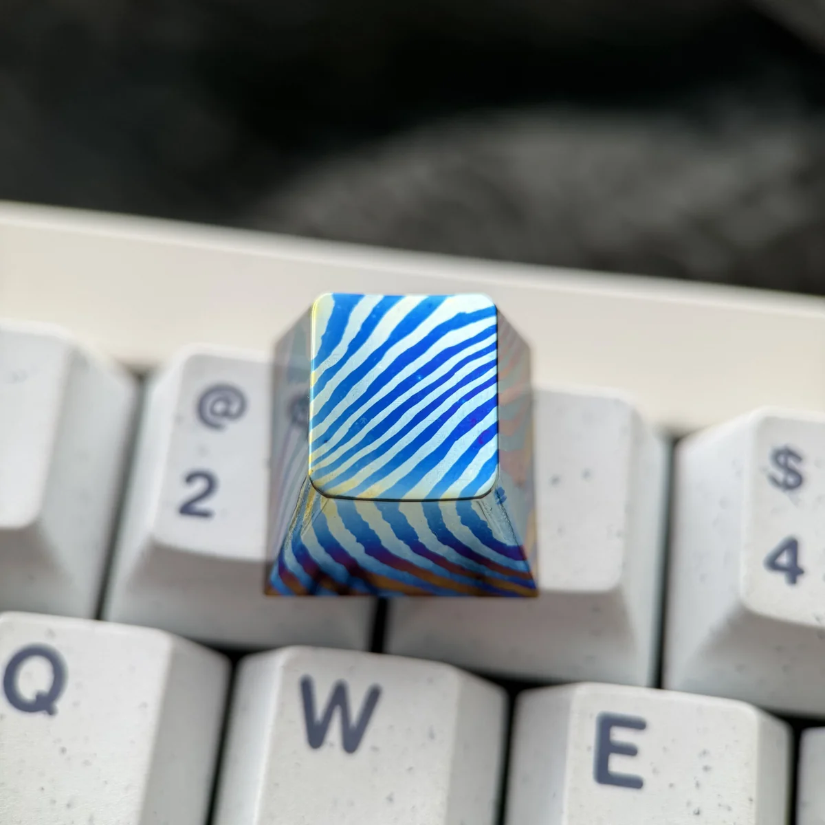 Close-up views of a unique handcrafted Damascus Titanium ESC keycap, showcasing its intricate patterns and iridescent titanium hues from multiple angles.