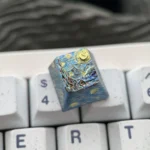 A close-up of the premium Van Gogh Starry Night Titanium ESC keycap, showcasing its cosmic blues, swirling yellows, and celestial artistry from a unique design.