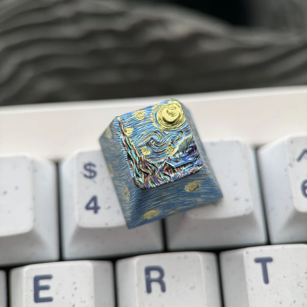 A close-up of the premium Van Gogh Starry Night Titanium ESC keycap, showcasing its cosmic blues, swirling yellows, and celestial artistry from a unique design.
