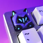 Playful Valorant Omen SA profile keycap with unique cat ear and paw design, shown from multiple angles against a shadowy, artistic background.