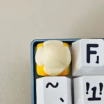 Detailed view of a whimsical handcrafted banana resin keycap, showcasing its vibrant yellow hue and miniature tropical fruit design, perfect for playful setup.