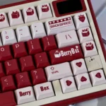 Charming Berry Box PBT Dye-Sub Keycap Set, shown from a playful angle. Highlights vibrant red strawberries and sweet box motifs for a delightful design.