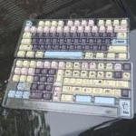 A close-up view of the DuCato Cherry Keycap Set, showcasing vibrant five-sided dye-sub legends with playful character art on multiple keys,