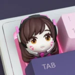 This handcrafted D.VA Overwatch artisan keycap shines with vibrant pinks and detailed resin, showcased from various angles to reveal its playful gaming setup.