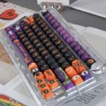 Vibrant Halloween PBT dye-sub keycaps set for mechanical keyboards, with playful spooky pumpkins, ghosts, and bats. The set is viewed from various angles.