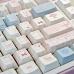 Elegant Rococo PBT Dye-Sub Keycap Set displayed from a side angle, highlighting its ornate pastel designs, intricate scrollwork, and delicate natural design.