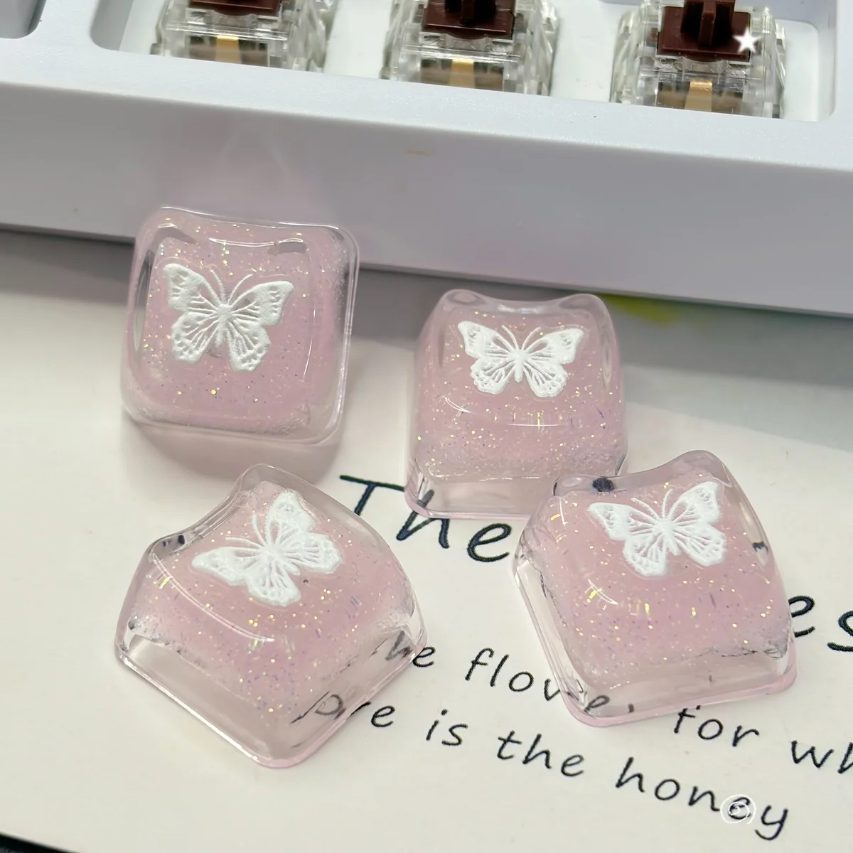 Ethereal pink butterfly resin keycap gallery, showing its handcrafted translucent design with shimmering glitter. Multiple angles reveal this dreamy design.