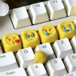 A delightful collection of playful handcrafted resin emoji keycaps, displayed from multiple angles to showcase their vibrant expressions, glossy finish.