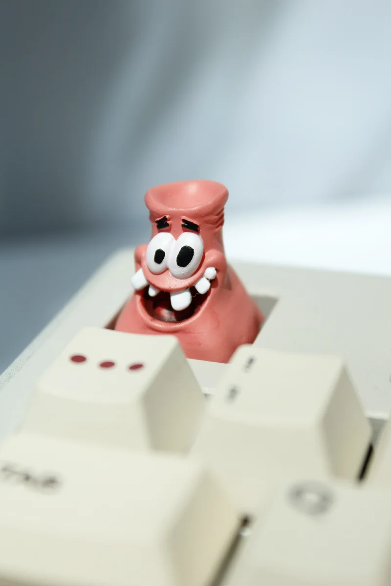 A vibrant, handcrafted Patrick Star artisan keycap for mechanical keyboards, showcasing its iconic, goofy design from multiple playful angles.