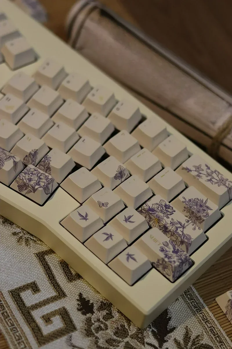 A collection of artisan embroidered PBT keycaps set, Cherry profile, Alice layout, displayed from various angles, revealing intricate textile art and vibrant design.