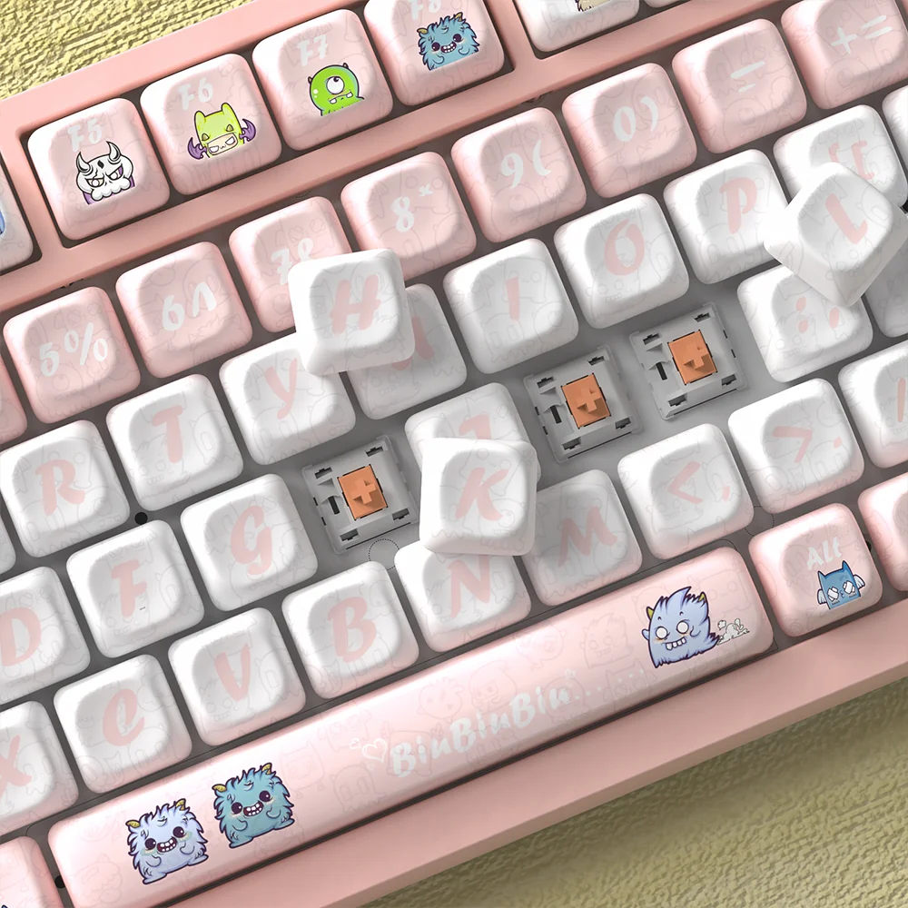 A collection of Strange Beast MOA PBT keycaps from various angles, showcasing their whimsical monster art and uniform ergonomic profile for comfortable.