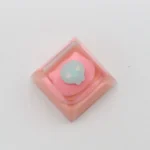 Whimsical pink cat keycap, handcrafted from luminous resin, shown from a playful, distinct angle, highlighting its adorable details. A charming keyboard.