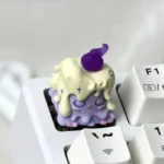 Whimsical 'Weaver of Light' ESC artisan keycap, handcrafted from unique resin, revealing its vibrant yellow and purple ethereal details from a captivating view.